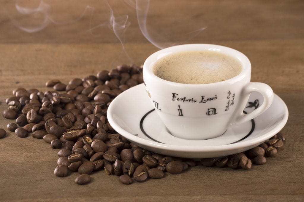 Une tasse de café expresso fumante et des grains de café étalés sur une table.